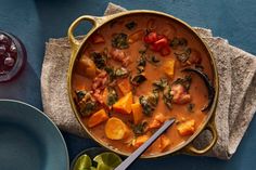 a pan filled with stew and vegetables on top of a blue tablecloth next to plates