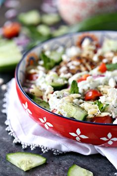 a salad with cucumbers and tomatoes in a red bowl on top of a table