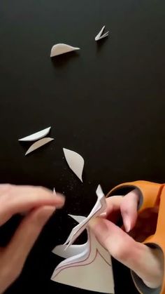 someone cutting paper with scissors on a black surface next to some pieces of white paper