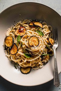 pasta with eggplant and parmesan cheese in a white bowl next to a fork