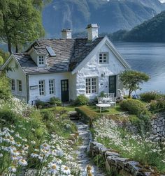 a white house sitting on top of a lush green hillside next to a body of water