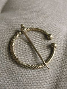 The fibula of brass Twisted Fibula Horseshoe shapes Brooch Scarf pin Ancient tribes Viking Jewelry Gift Historical Reenactment Pin. Brooch made of raw 3mm brass wire, hand hammered and forged. Made to order just for you An archaeological founding of Eastern Europe inspires this handcraft. Brooches similar to this were very common in the medieval period. Pinning method: insert the needle into the fabric, set the aperture on the needle, and then rotate the circle by passing behind the tip. Antique Gold Brass Brooch, Brooch Scarf, Viking Reenactment, Historical Reenactment, Scarf Rings, Fabric Set, Medieval Jewelry, Scarf Pin, Medieval Period