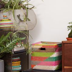 a stack of multicolored baskets sitting on top of a wooden table next to a potted plant