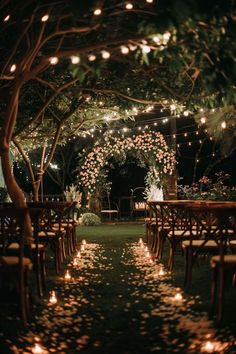 an outdoor wedding venue with candles lit up in the trees and flowers on the ground