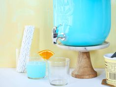 a blue ice bucket sitting on top of a table next to two glasses and an orange slice