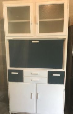 a white cabinet with two doors and some drawers on the bottom, in front of a wall