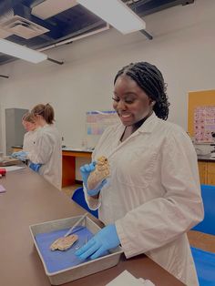 two women in white lab coats and blue gloves are standing at a table with food