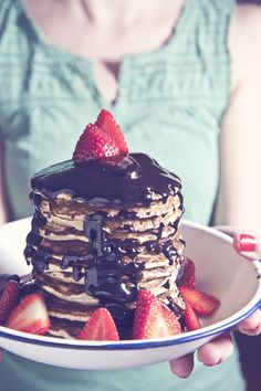 a woman holding a plate with pancakes and strawberries