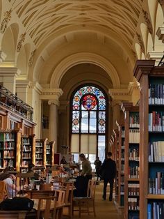 people are sitting at tables in the library with bookshelves and stained glass windows