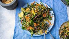 a salad with carrots, onions and greens on a blue cloth next to two bowls