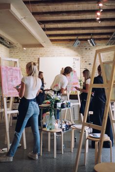 a group of people standing around in a room with easels and paintings on the walls