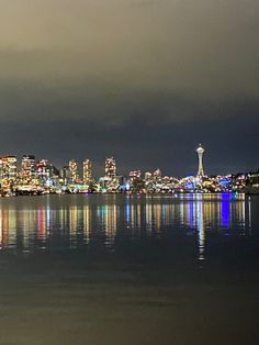 the city lights are reflected in the still water on the lake's surface, while dark clouds loom over the skyline