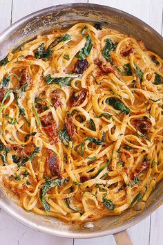 a pan filled with pasta and spinach on top of a wooden table