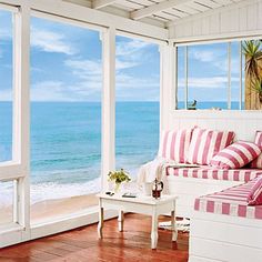 a living room filled with furniture next to an ocean front window covered in pink and white striped pillows