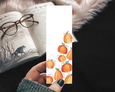 a person holding an open book with oranges on it and reading glasses next to them