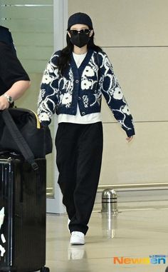 a woman wearing a face mask walks through an airport with her luggage and another man in the background