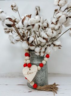 a vase filled with cotton flowers and a wooden heart hanging from it's side