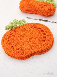 two crocheted pumpkins sitting on top of a table next to knitting needles