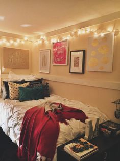 an unmade bed with lights strung from the ceiling and pictures on the wall above it