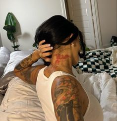 a woman with tattoos on her back sitting on a bed in front of a mirror