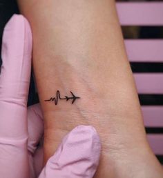 a small tattoo on the wrist with an arrow and heartbeat beat sign in black ink