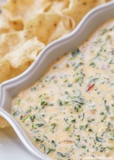 a white bowl filled with cheese and spinach dip next to chips on a plate