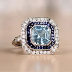 This platinum ring features a 1.97 carat aquamarine in an Asscher cut. It is surrounded by a halo of calibrated French cut sapphires, as well as a second halo of round brilliant cut diamonds. Additional round brilliant cut diamonds adorn the shoulders. The total weight of the diamonds is approximately 0.51 carats. This ring is embellished with fine milgrain and an open-work under-gallery.
The approximate dimensions of the aquamarine are 8.00mm x 8.00mm. The measurements of this ring are approxim Diamond Ring With Halo, Asscher Cut Diamond Ring, Ring With Halo, Asscher Cut Ring, Estate Diamond Jewelry, Aquamarine Engagement Ring, French Cut, Aquamarine Jewelry, Aquamarine Ring