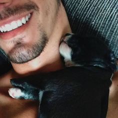 a man holding a small black and white dog in his arms while smiling at the camera