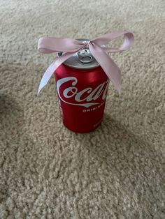 a coca cola can with a pink ribbon tied around it on top of the carpet