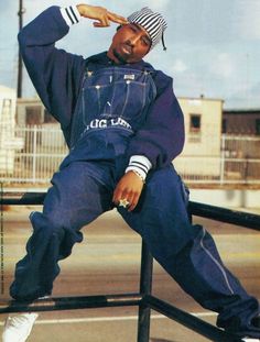 a man sitting on top of a metal rail wearing overalls and a striped hat