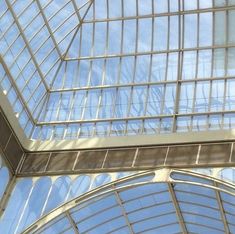 the inside of a building that has glass walls and windows on each side, looking up into the sky