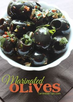 a bowl filled with black olives sitting on top of a wooden table next to a napkin