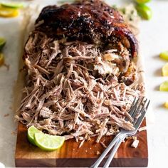 a wooden cutting board topped with meat covered in sauce and garnished with lime wedges