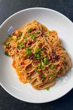 a white plate topped with noodles and vegetables on top of a black countertop next to a fork