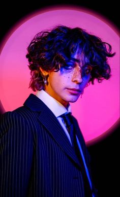 a woman with curly hair wearing a suit in front of a pink and blue background