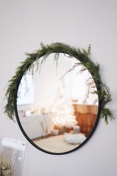 a round mirror hanging on the wall above a table with a christmas tree in it