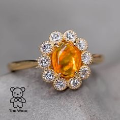 an orange and white diamond ring sitting on top of a stone surface with a teddy bear in the background