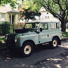 an old green land rover is parked on the side of the road in front of a house