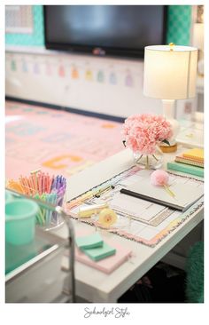 a white desk topped with a lamp next to a pink flower and notebooks on top of it