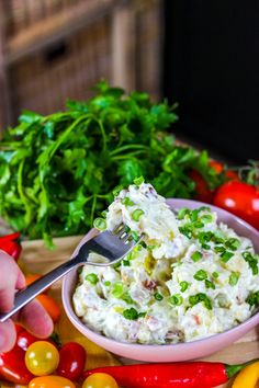 a person holding a fork over a bowl of food on a table with peppers and other vegetables