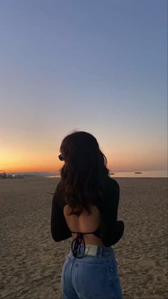 a woman standing on top of a sandy beach next to the ocean with her back turned