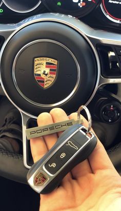 a hand holding a car key in front of a steering wheel with the emblem on it