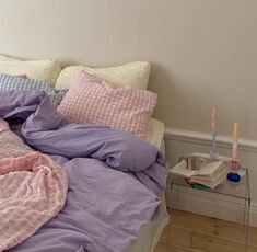 an unmade bed with pink and blue sheets on it, next to a night stand