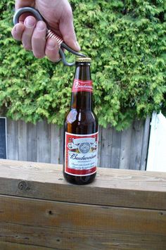 a bottle opener being used to open a beer bottle on a wooden table outside with trees in the background