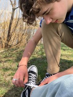 a young boy sitting on the ground tying his shoelaces to another person's shoes