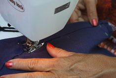 a woman is using a sewing machine to sew on her t - shirt with red nail polish