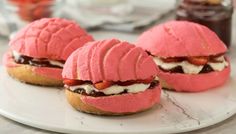 three pink frosted sandwiches on a plate with strawberries and cream in the background