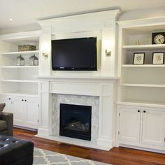 a living room with white bookcases and a flat screen tv above the fireplace