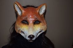 a woman wearing a fake fox mask with long black hair and orange paint on her face