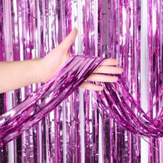 a woman's hand is holding pink streamers in front of purple tinsel